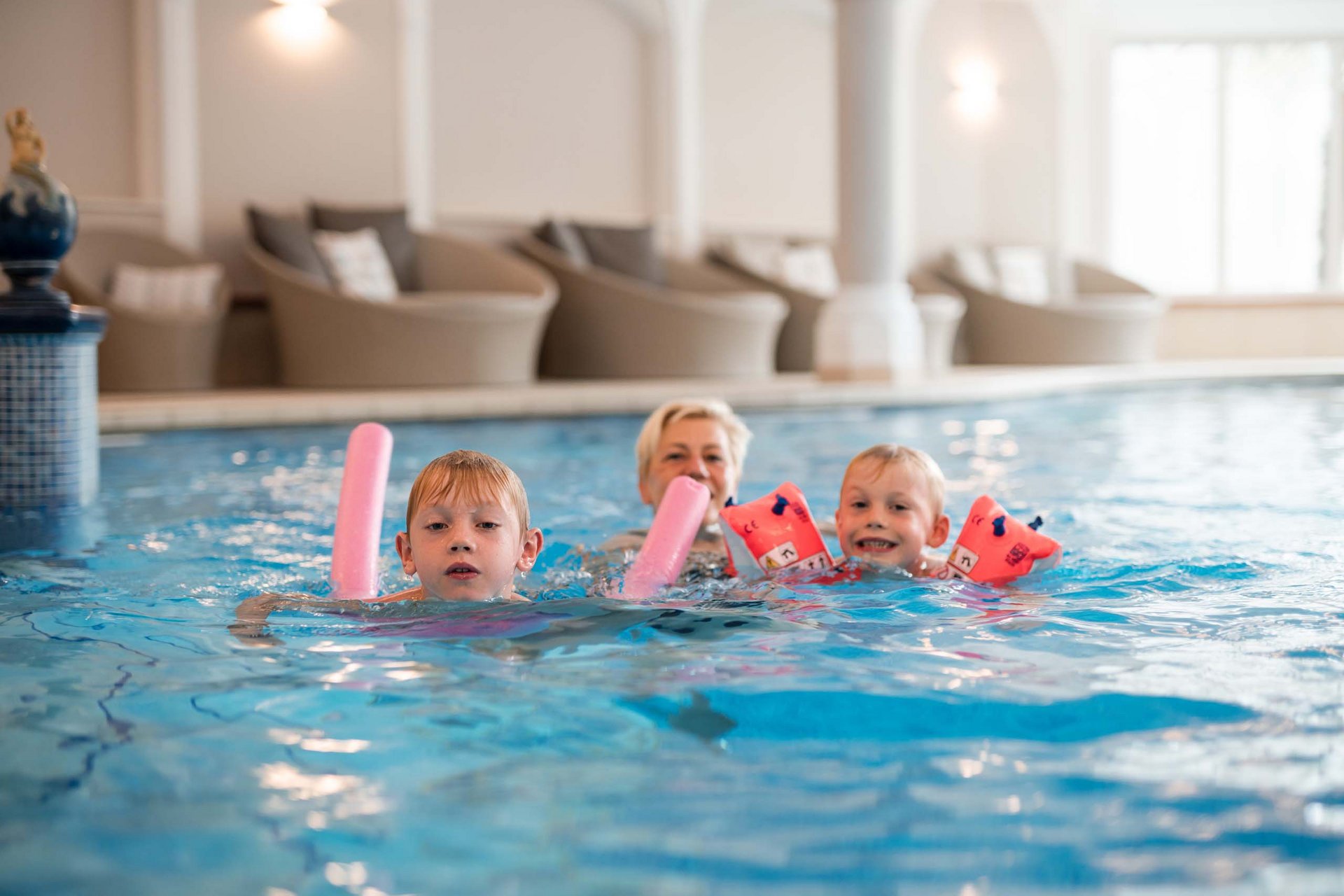 Schwimmen lernen im Urlaub Zwei Jungen und eine Frau planschen in einem Hallenbad mit Schwimmhilfen