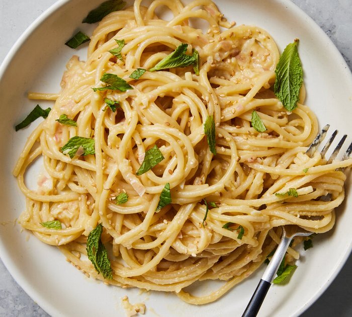 Spaghetti with creamy sauce topped with fresh mint leaves on white plate