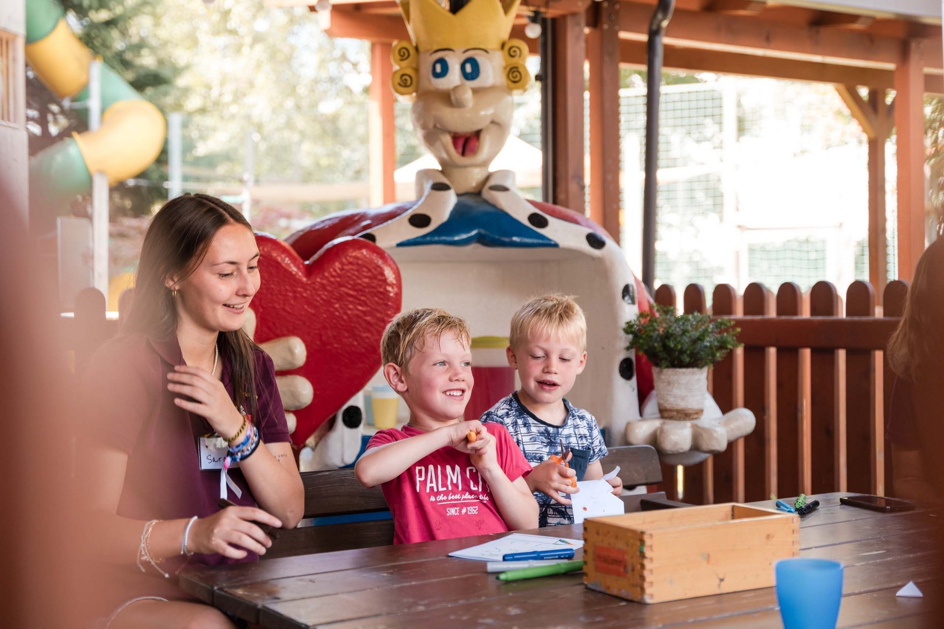 Das Animationsprogramm in König Pipos Kinderwelt Kinder basteln unter Anleitung neben einer großen Herzfigur im Freien
