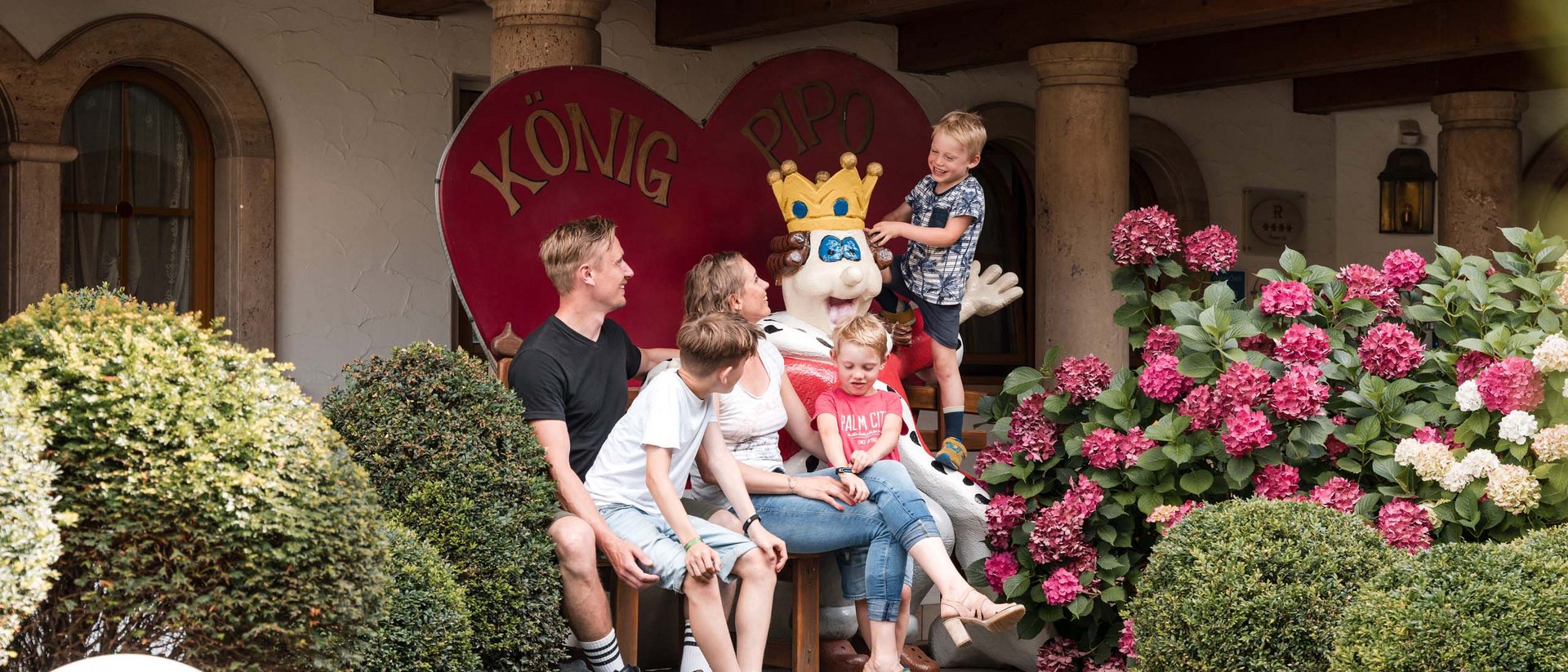 Das Animationsprogramm in König Pipos Kinderwelt Familie mit drei Kindern sitzt neben einer königlichen Figur im Garten