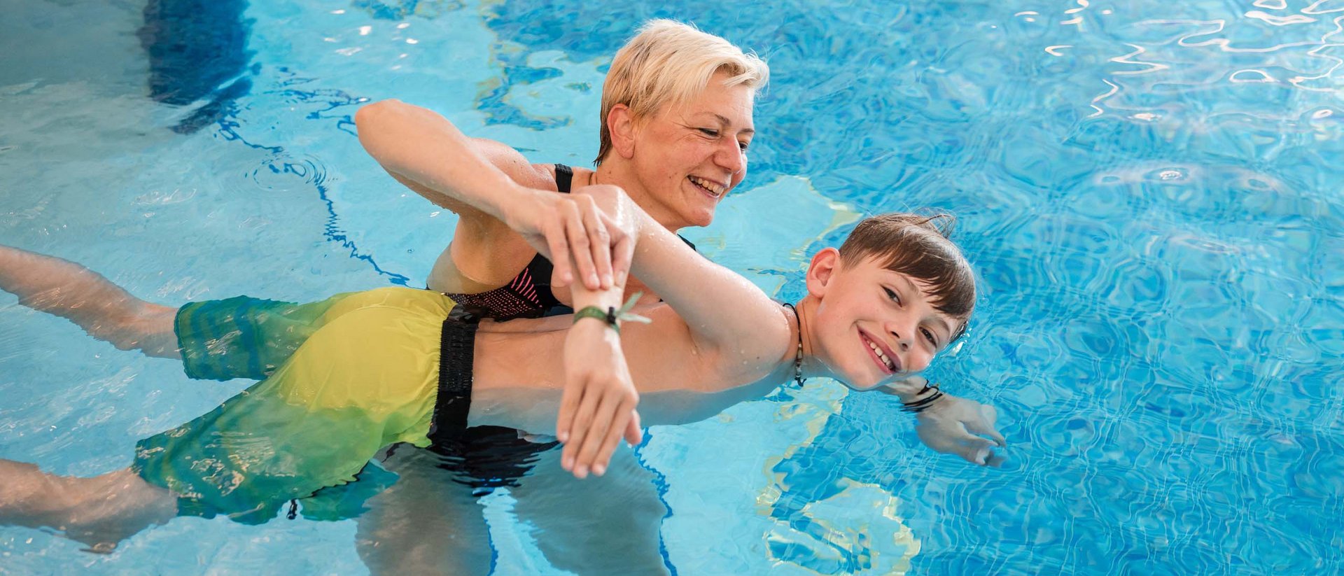 Schwimmen lernen im Urlaub Frau bringt Jungen im Schwimmbad Schwimmbewegungen bei