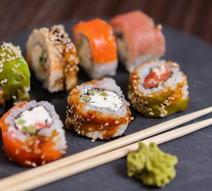 Assorted sushi rolls with wasabi and chopsticks on a black plate