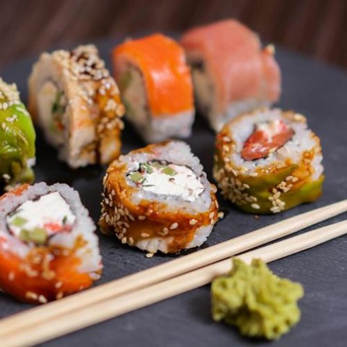 Assorted sushi rolls with wasabi and chopsticks on a black plate