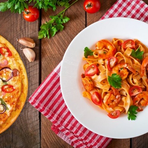 Pizza and shrimp pasta on wooden table with herbs and cherry tomatoes