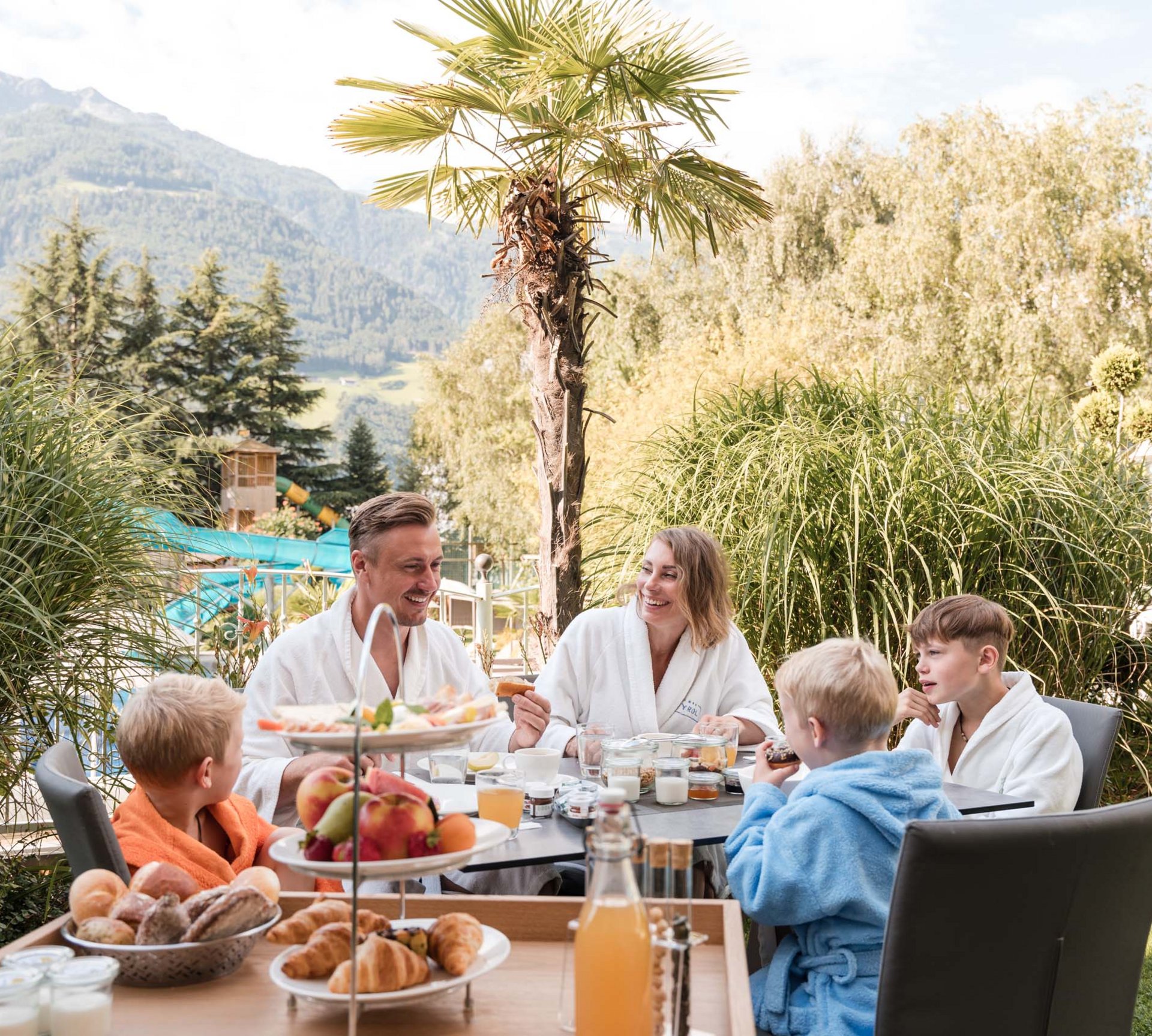 Famiglia fa colazione all'aperto con montagne e palme sullo sfondo