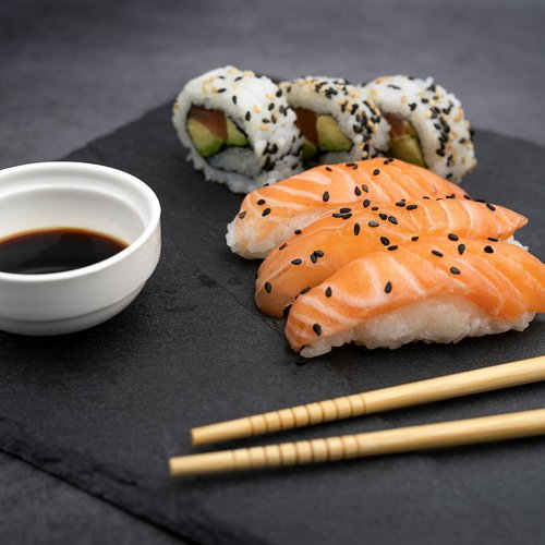 Sushi with salmon, California rolls, soy sauce and chopsticks on black slate