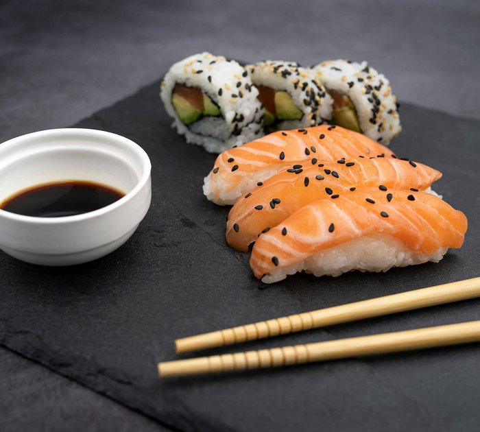 Sushi with salmon, California rolls, soy sauce and chopsticks on black slate
