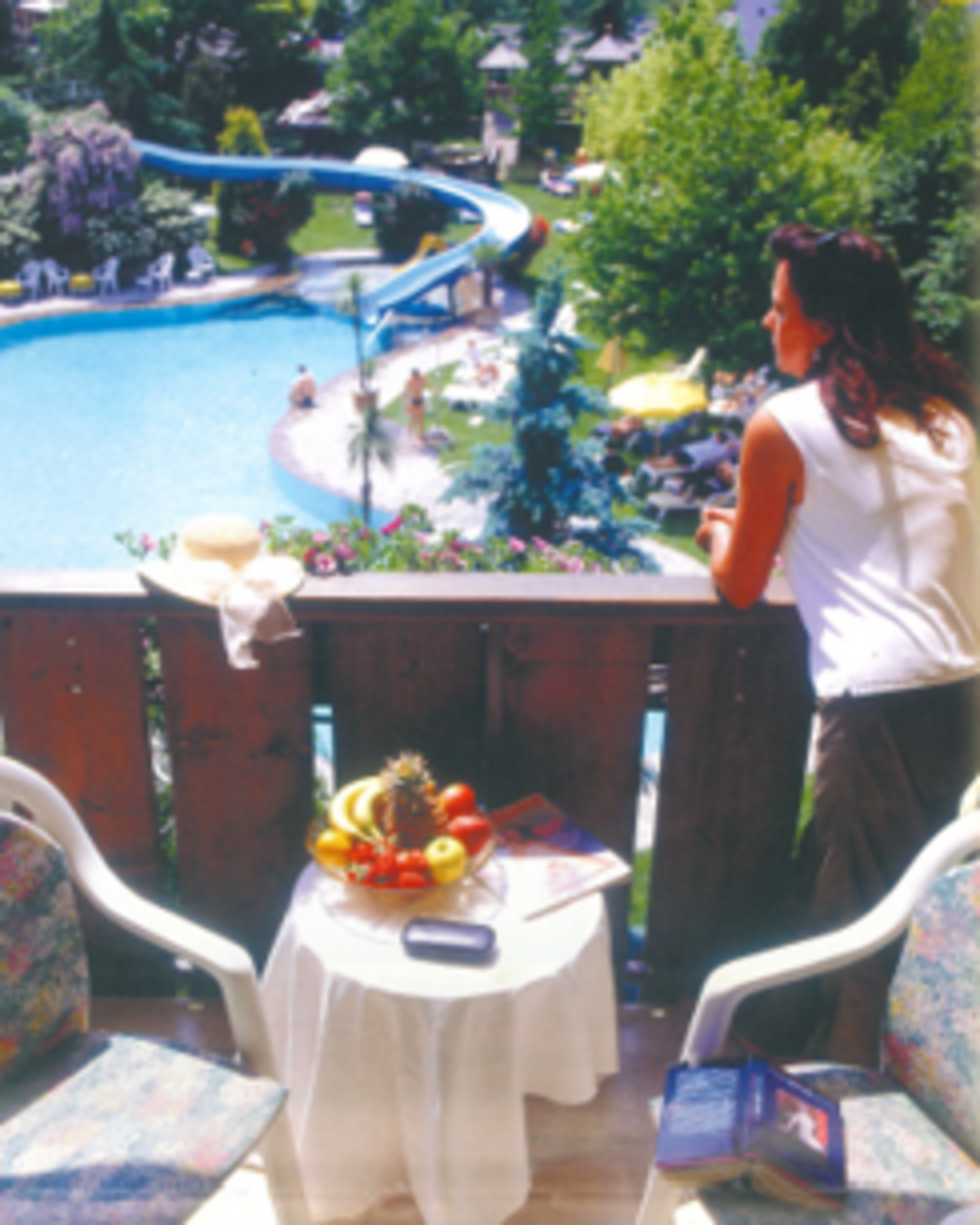 Donna sul balcone guarda piscina con scivolo in parco verde