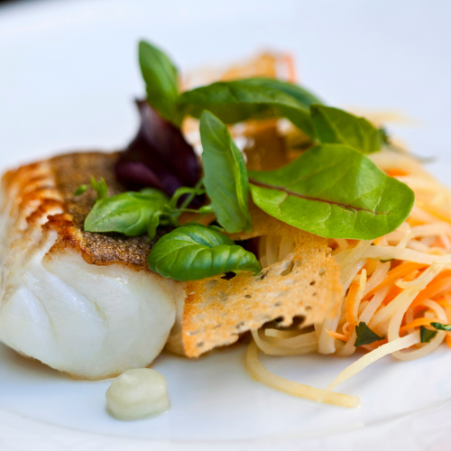 Gebratenes Fischfilet mit frischen Kräutern und Gemüsesalat auf weißem Teller