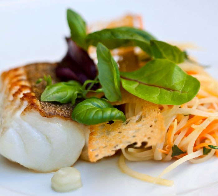Gebratenes Fischfilet mit frischen Kräutern und Gemüsesalat auf weißem Teller
