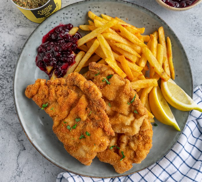 Breaded schnitzel with fries, lemon wedges, and lingonberry sauce on a plate