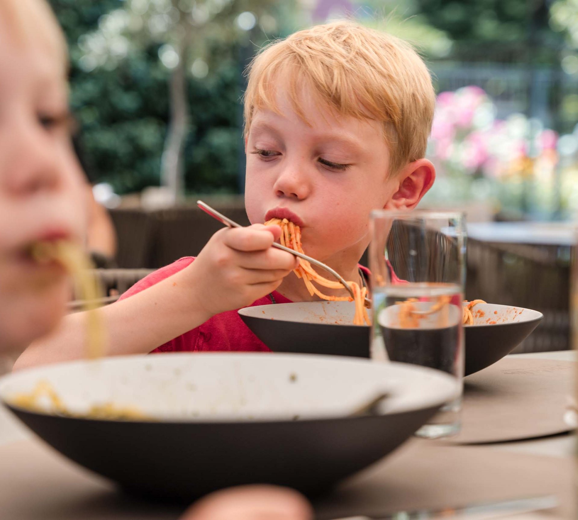 Two boys eating spaghetti at an outdoor table
