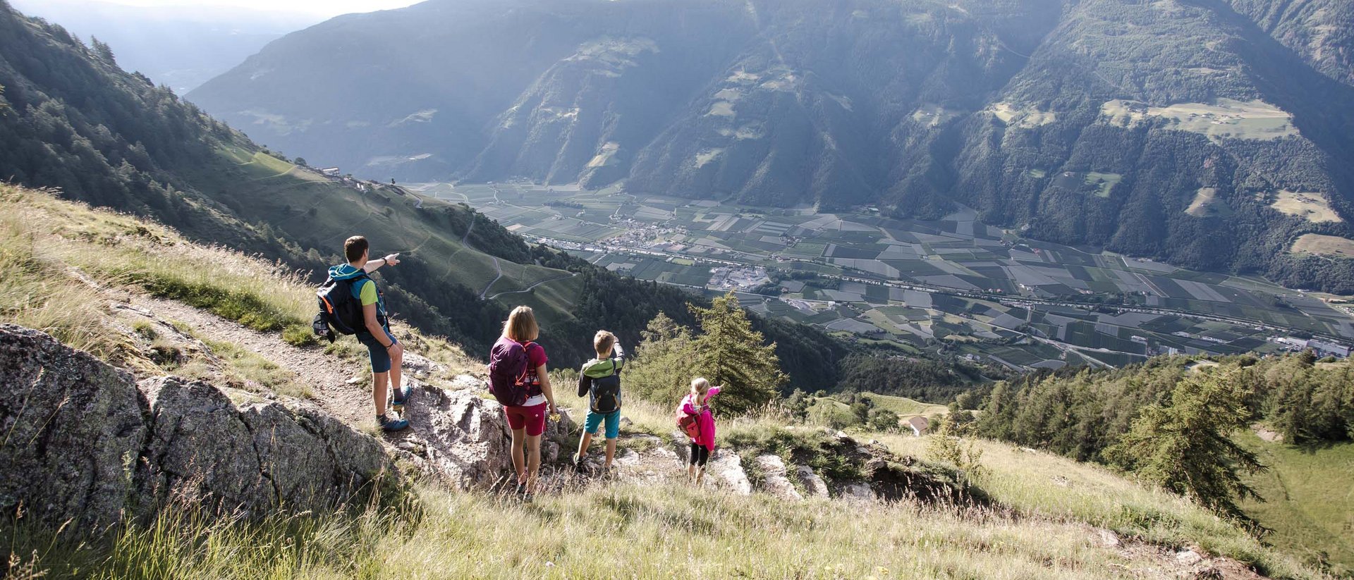 Familie wandert auf Bergweg mit Blick auf Tal und Berge