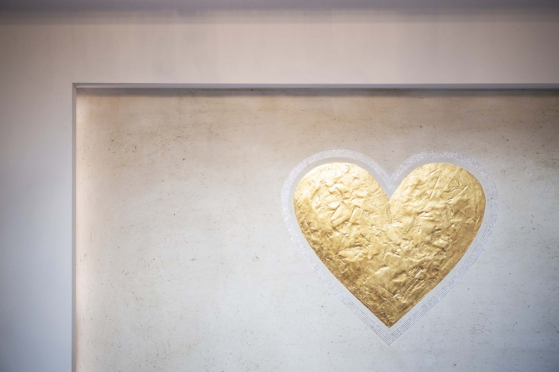 Goldenes Herzrelief an einer hellen Wand
