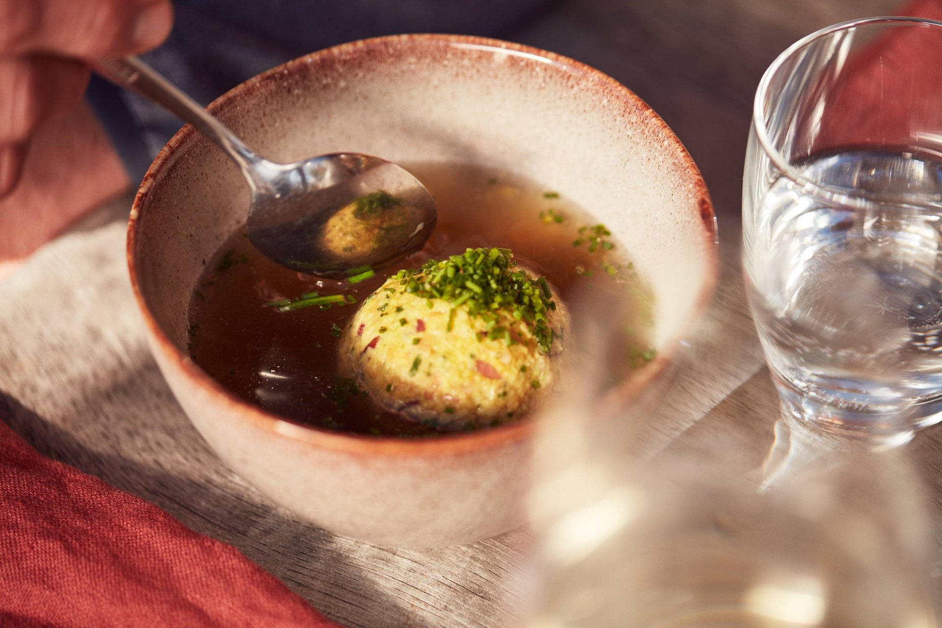Törggele-Zauber und Herbstgenuss Schale mit Bouillon und Semmelknödel, daneben ein Glas Wasser