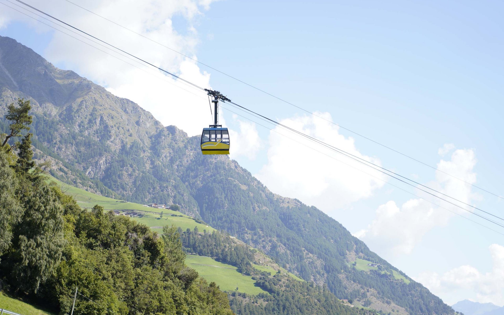 Seilbahn fährt über grüne Alpenlandschaft mit Bergen und blauem Himmel