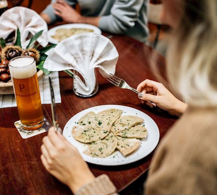 Frau isst Ravioli mit Bier an einem gedeckten Holztisch.