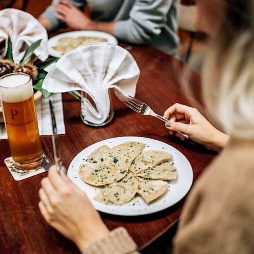 Frau isst Ravioli mit Bier an einem gedeckten Holztisch.