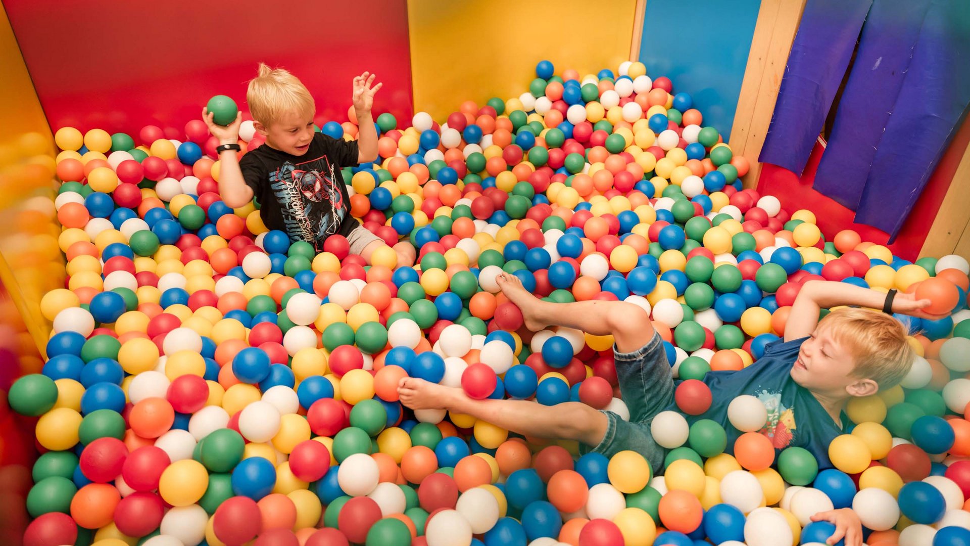 Zwei Jungen spielen in einem Bällebad mit bunten Kunststoffbällen