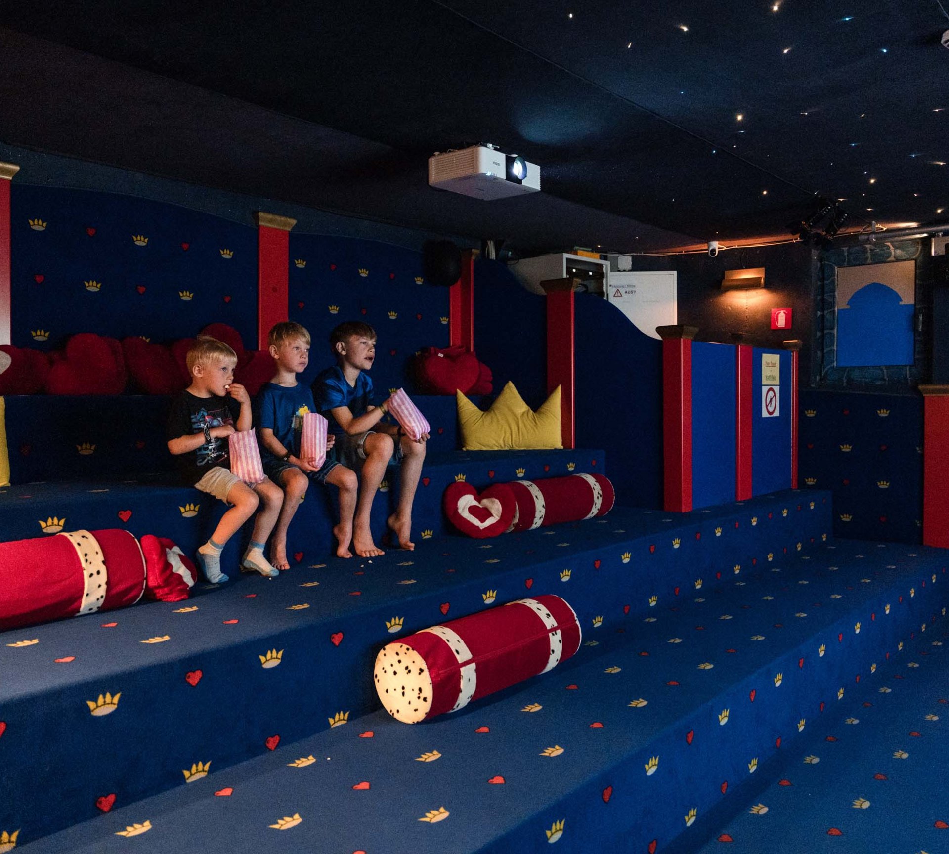 Tre ragazzi seduti in una piccola sala cinema colorata che mangiano popcorn
