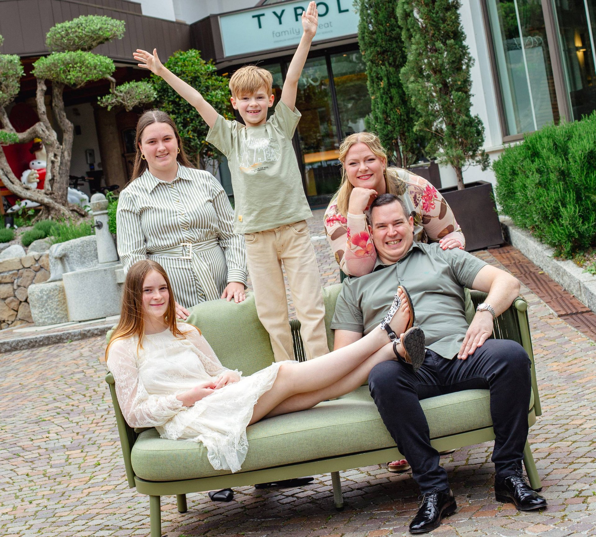 Famiglia felice con due bambini davanti all'hotel Tyrol su divano verde