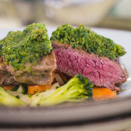 Juicy steak with green herb crust and vegetables on white plate