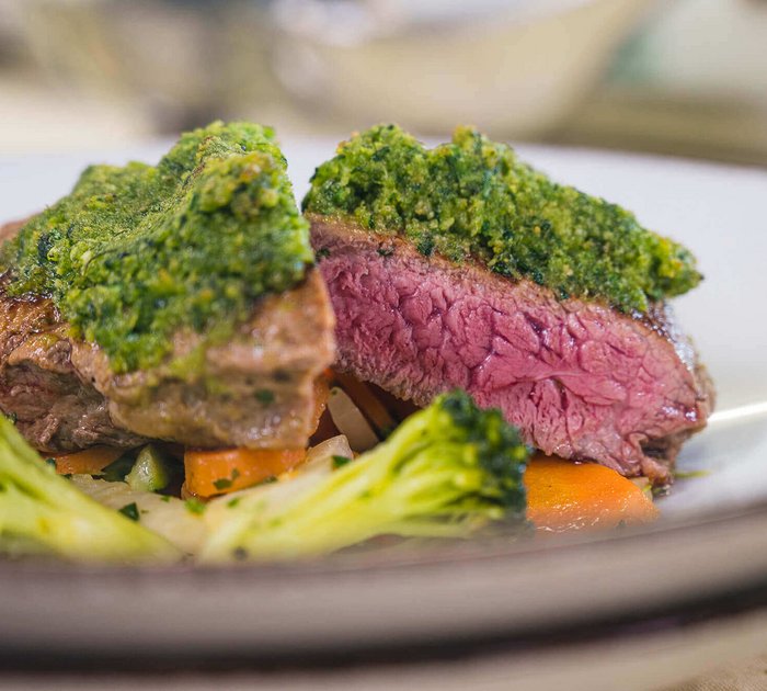 Juicy steak with green herb crust and vegetables on white plate
