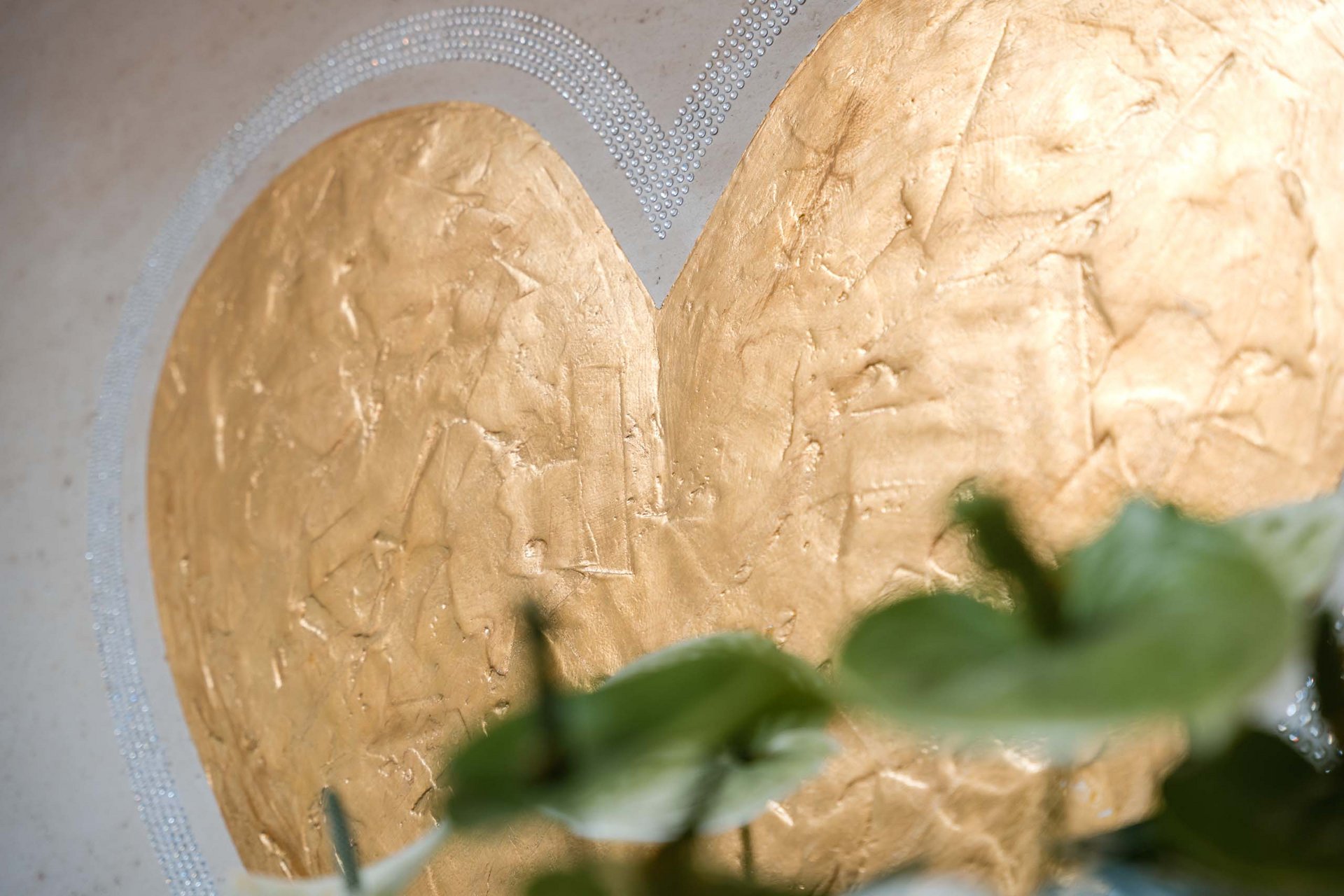 Close-up of golden heart artwork with green leaves in the foreground