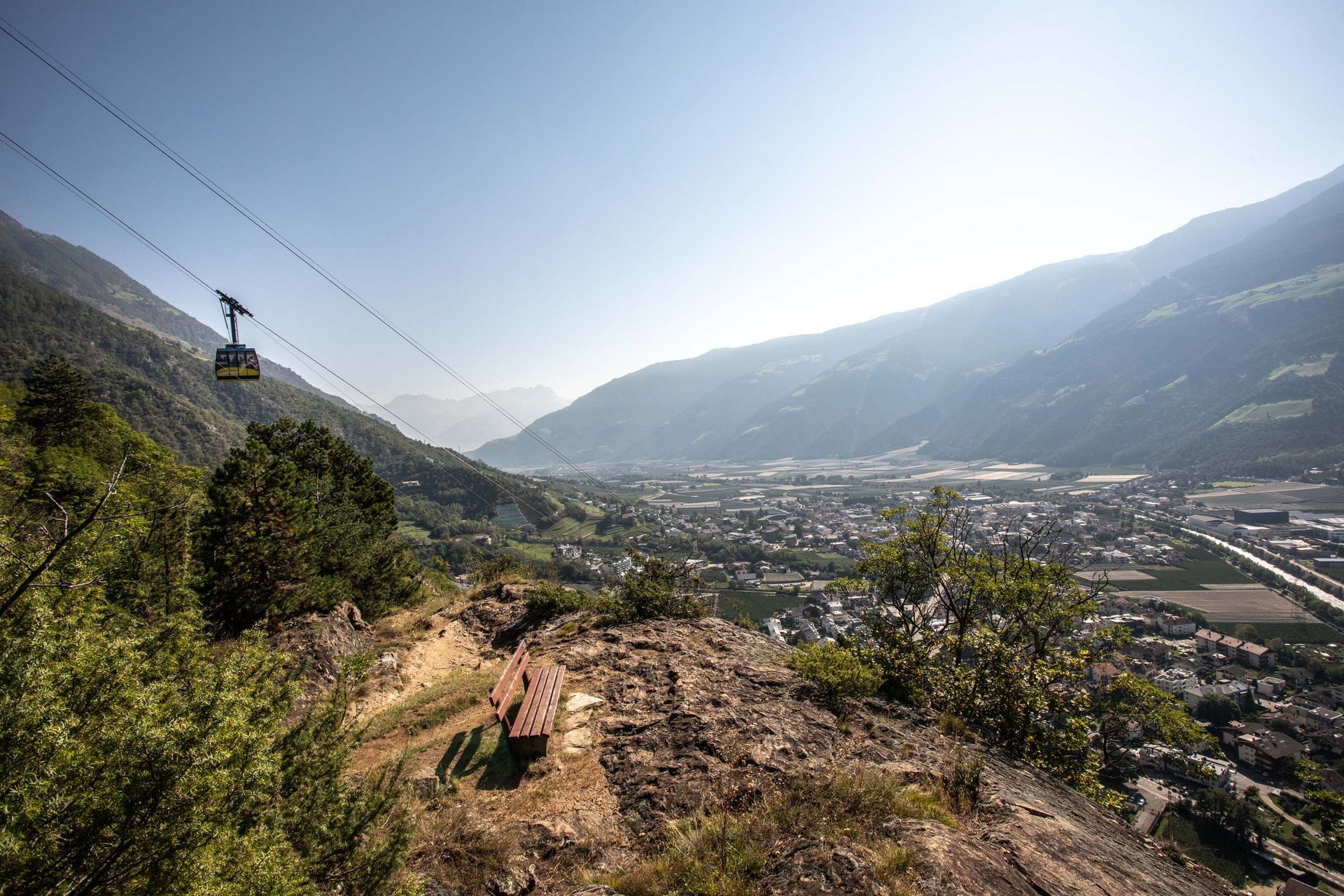 Die schönsten Aussichtsplätze für euch Bank auf Felsen mit Blick auf Tal und Seilbahn in den Bergen