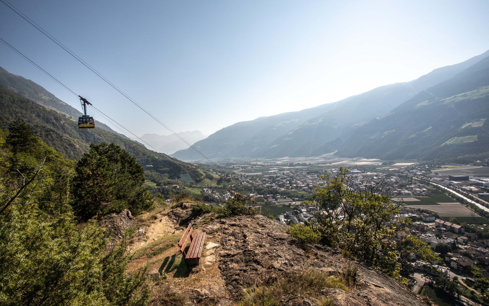 Bank auf Felsen mit Blick auf Tal und Seilbahn in den Bergen