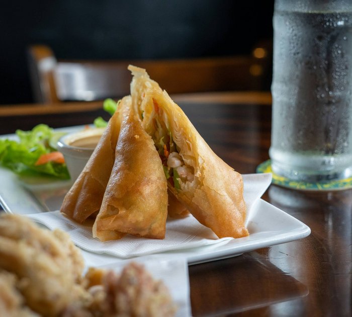Crispy spring rolls on a white plate with dipping sauce and a glass of water