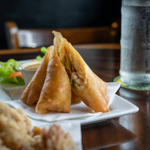 Crispy spring rolls on a white plate with dipping sauce and a glass of water