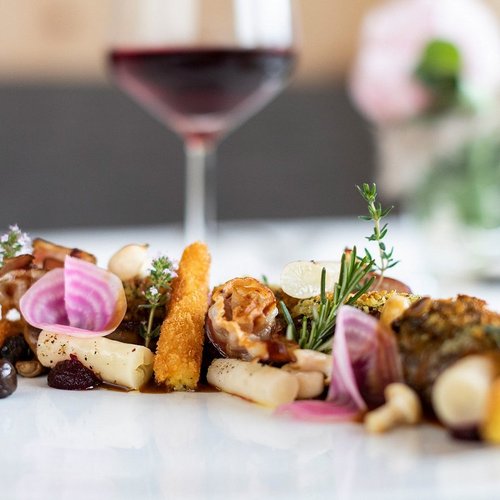 Gourmet-Gemüseplatte mit frischen Kräutern und Rotwein im Hintergrund