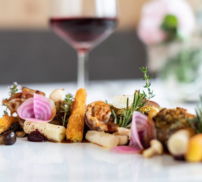 Gourmet-Gemüseplatte mit frischen Kräutern und Rotwein im Hintergrund