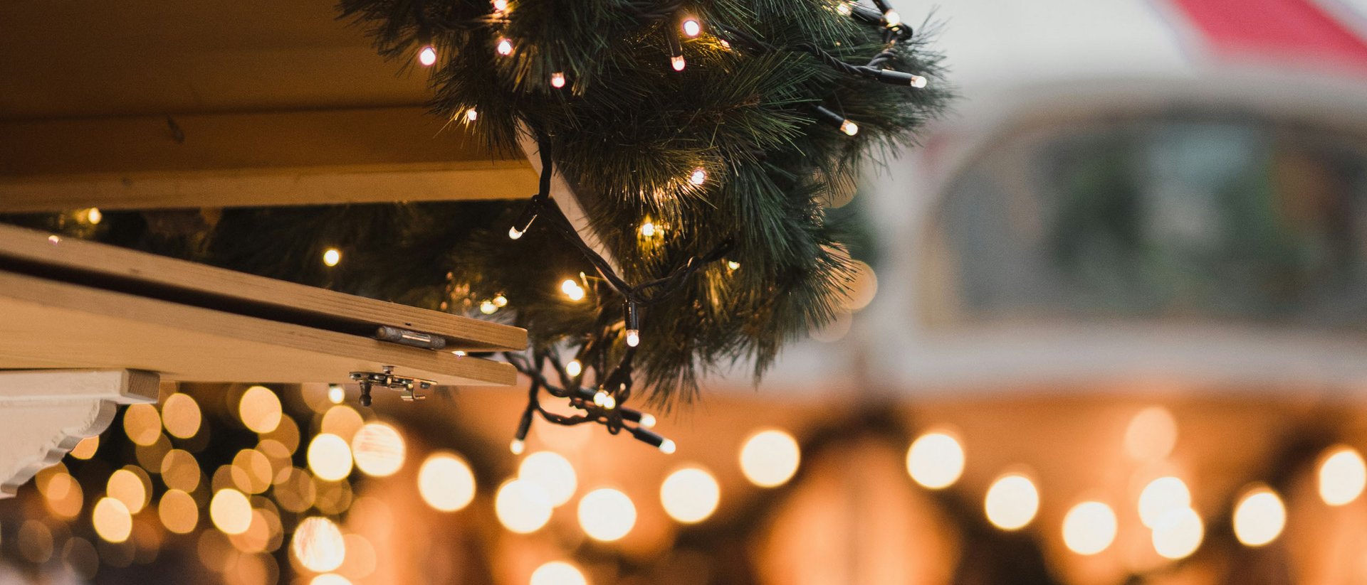 Weihnachtsbeleuchtung und Tannenzweige auf einem Markt mit unscharfem Karussell