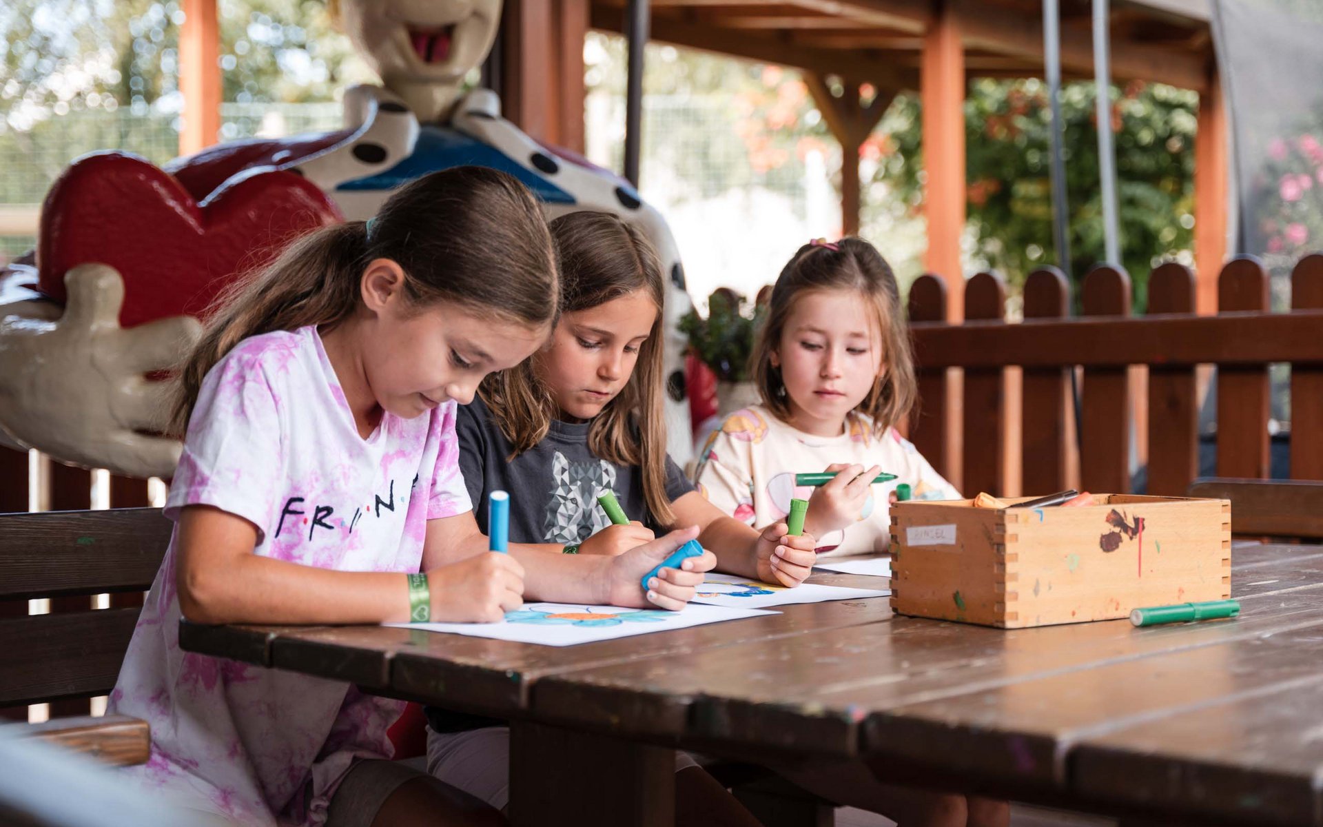 Drei Mädchen sitzen am Tisch und malen mit Stiften auf Papier