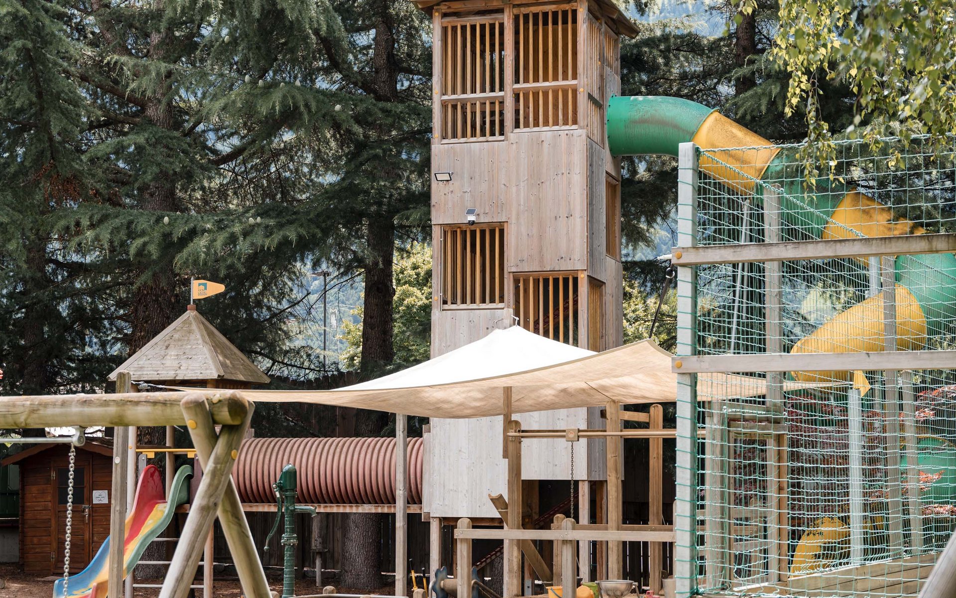 Kinderspielplatz mit Holzspielturm, Rutsche und Schaukel umgeben von Bäumen