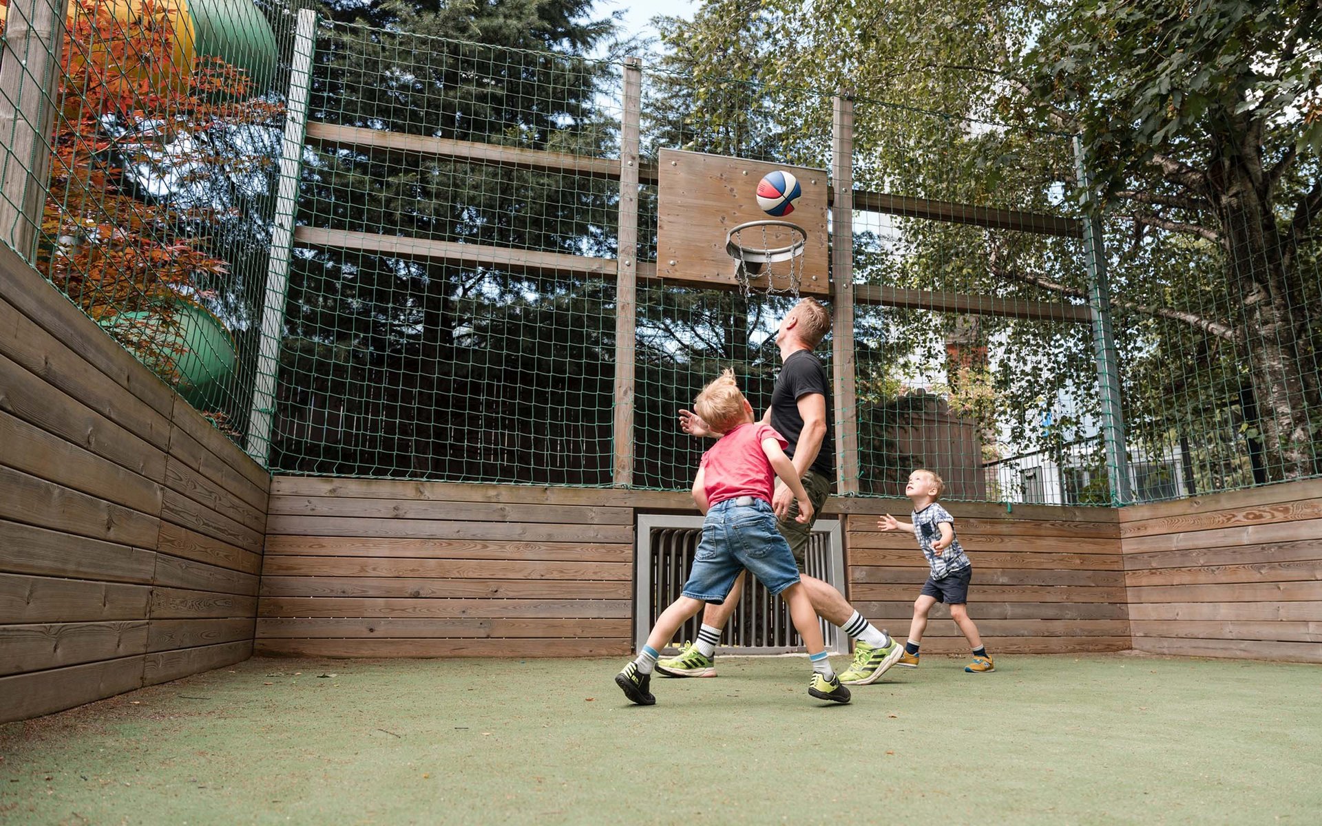 Vater und zwei Kinder spielen Basketball im Außenbereich