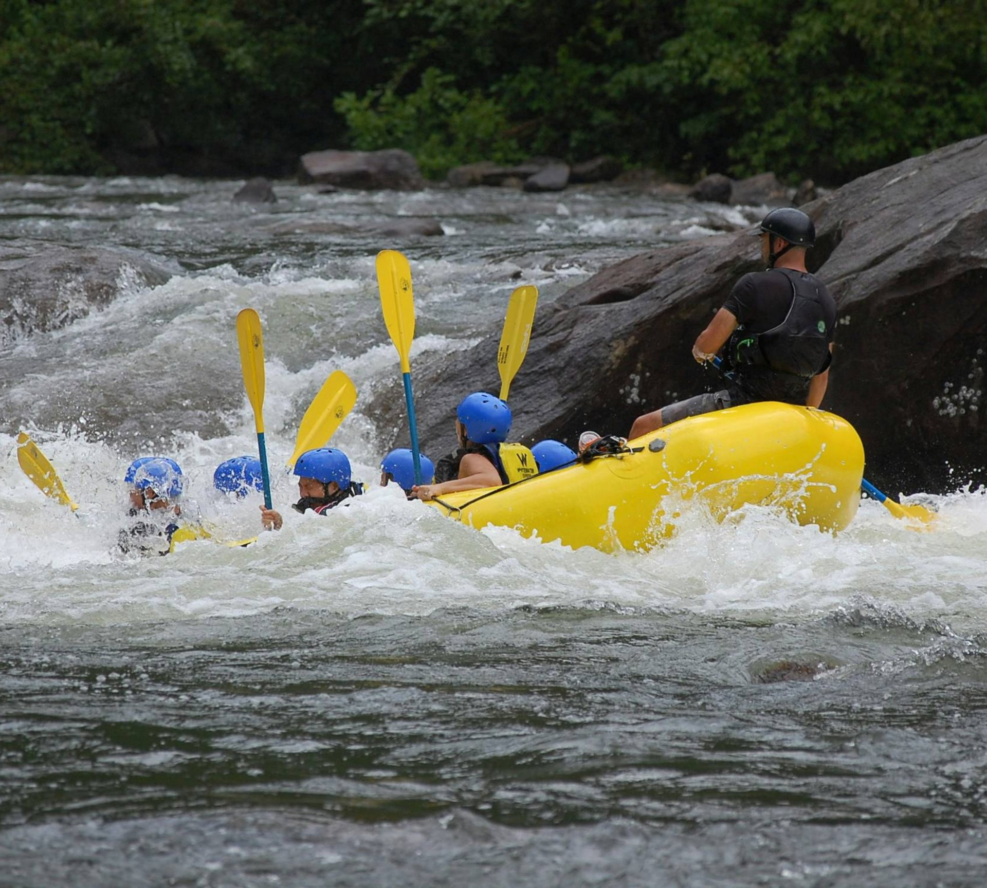 Group whitewater rafting on a river with blue helmets and yellow paddles