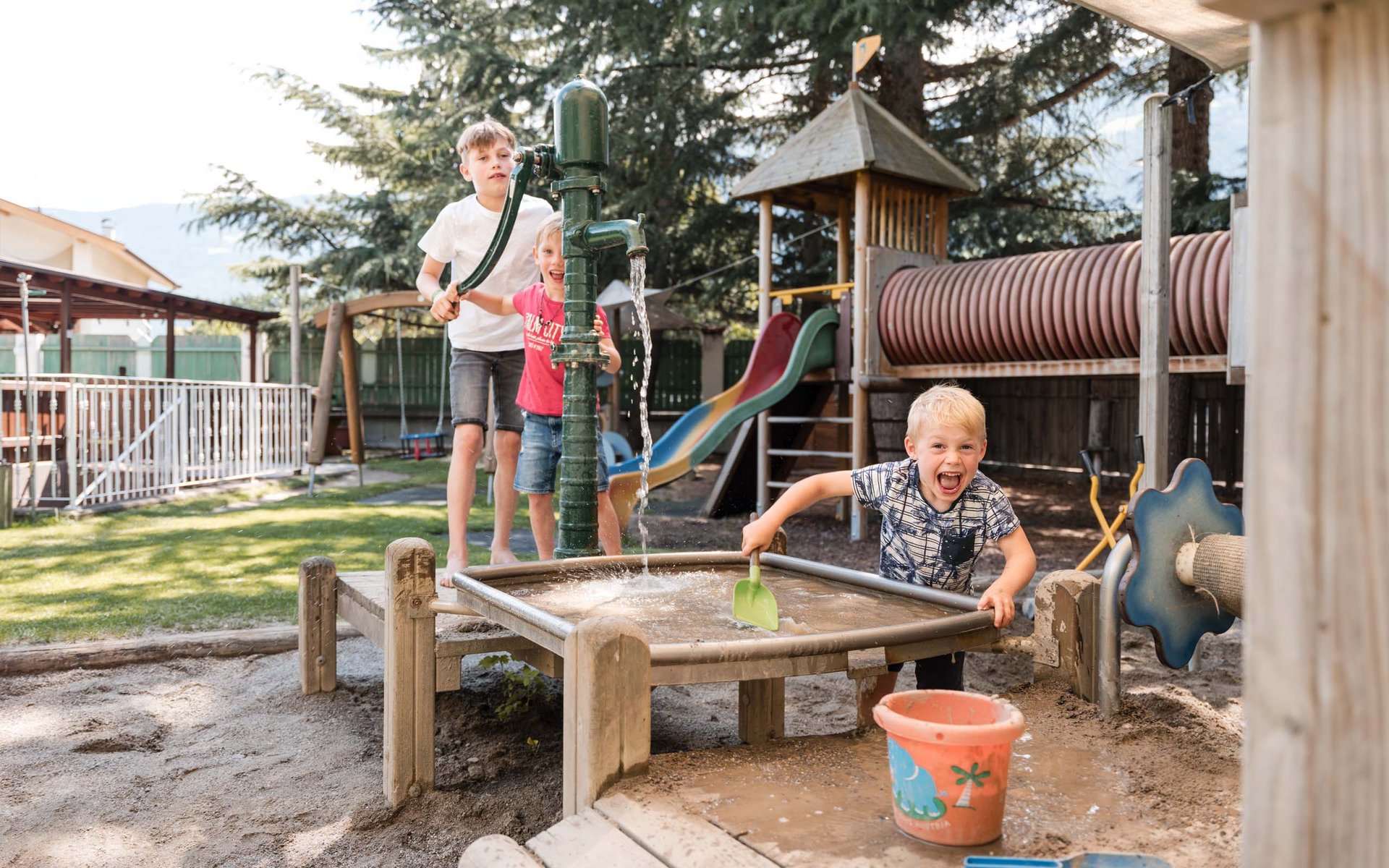Kinder spielen mit Wasserpumpe und Sand im Spielplatz mit Rutsche