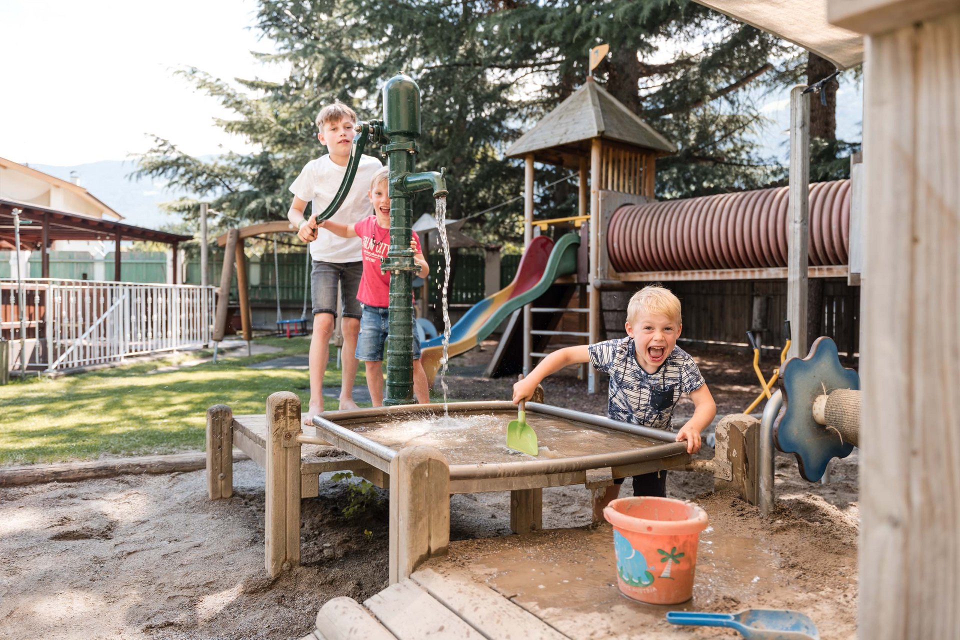 Children playing with water pump and sand in playground with slide