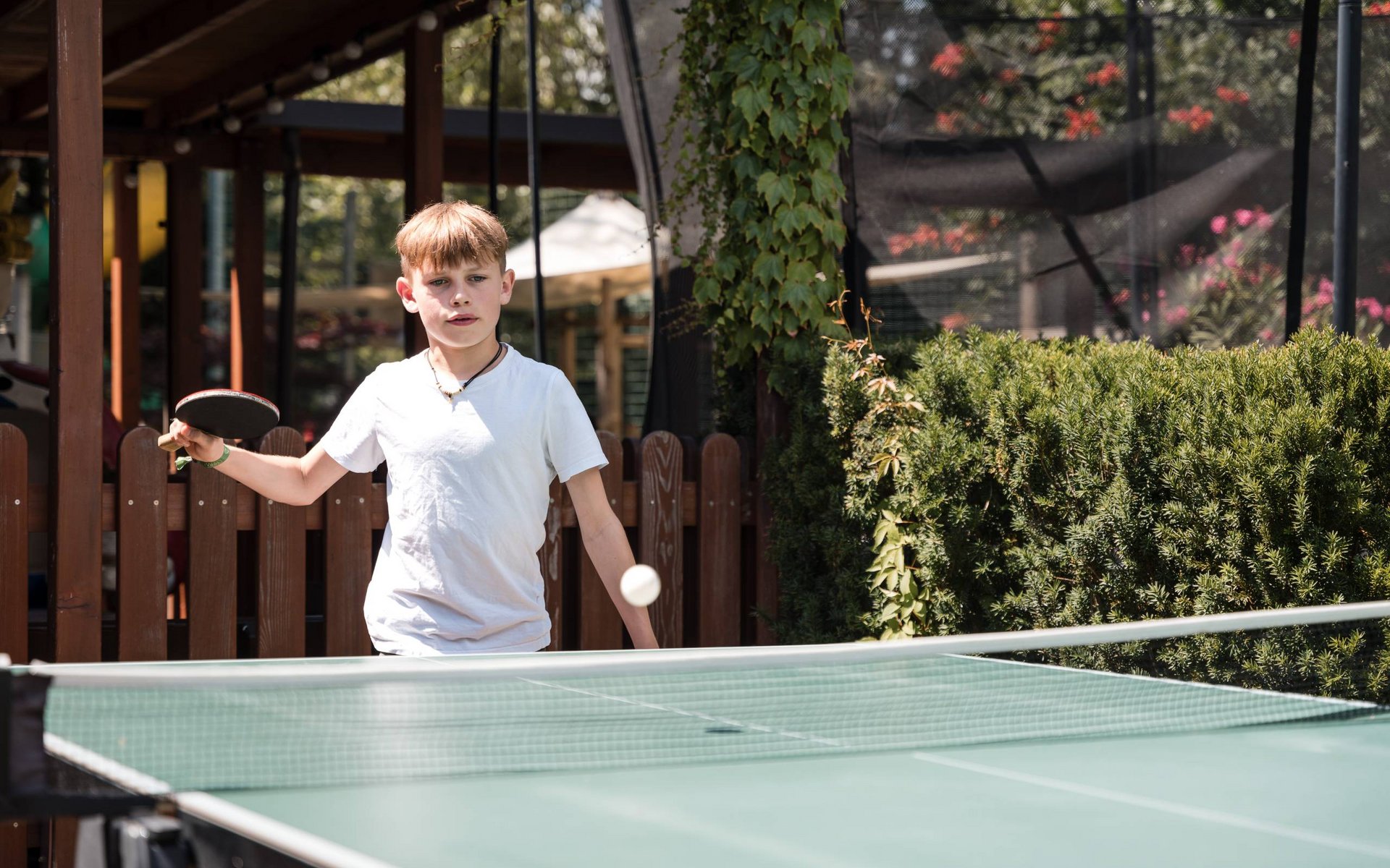Junge spielt Tischtennis im Freien mit grünem Tisch und Umgebungsbepflanzung