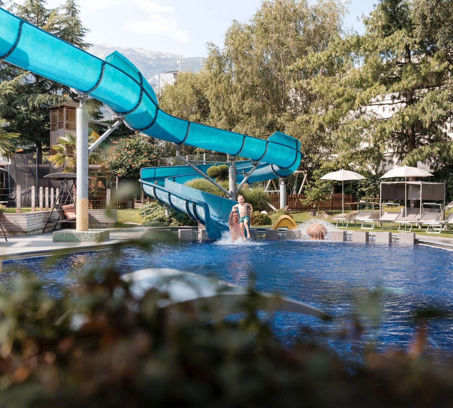 Vater und Kind springen ins Schwimmbecken von Wasserrutsche im Garten