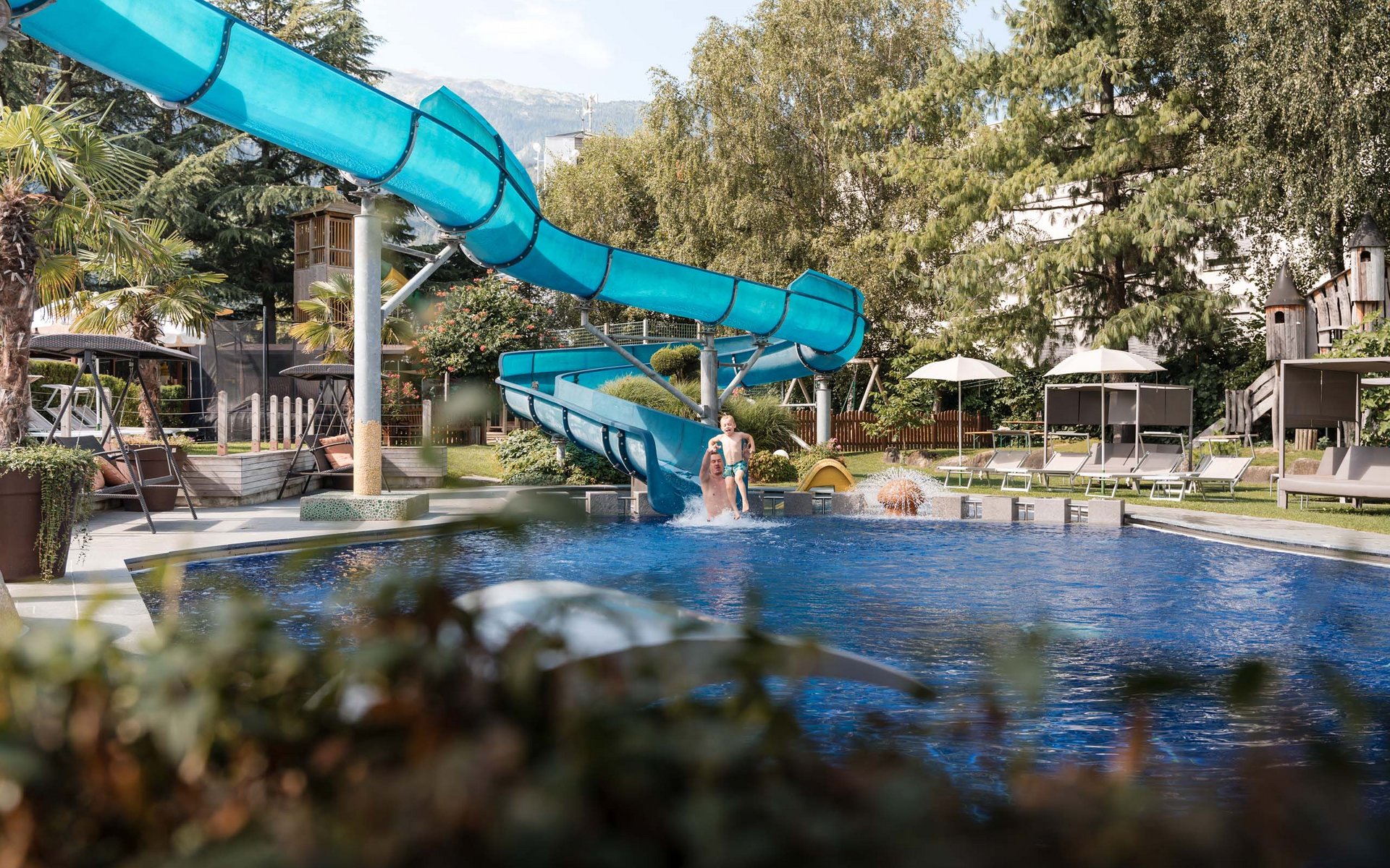 Vater und Kind springen ins Schwimmbecken von Wasserrutsche im Garten