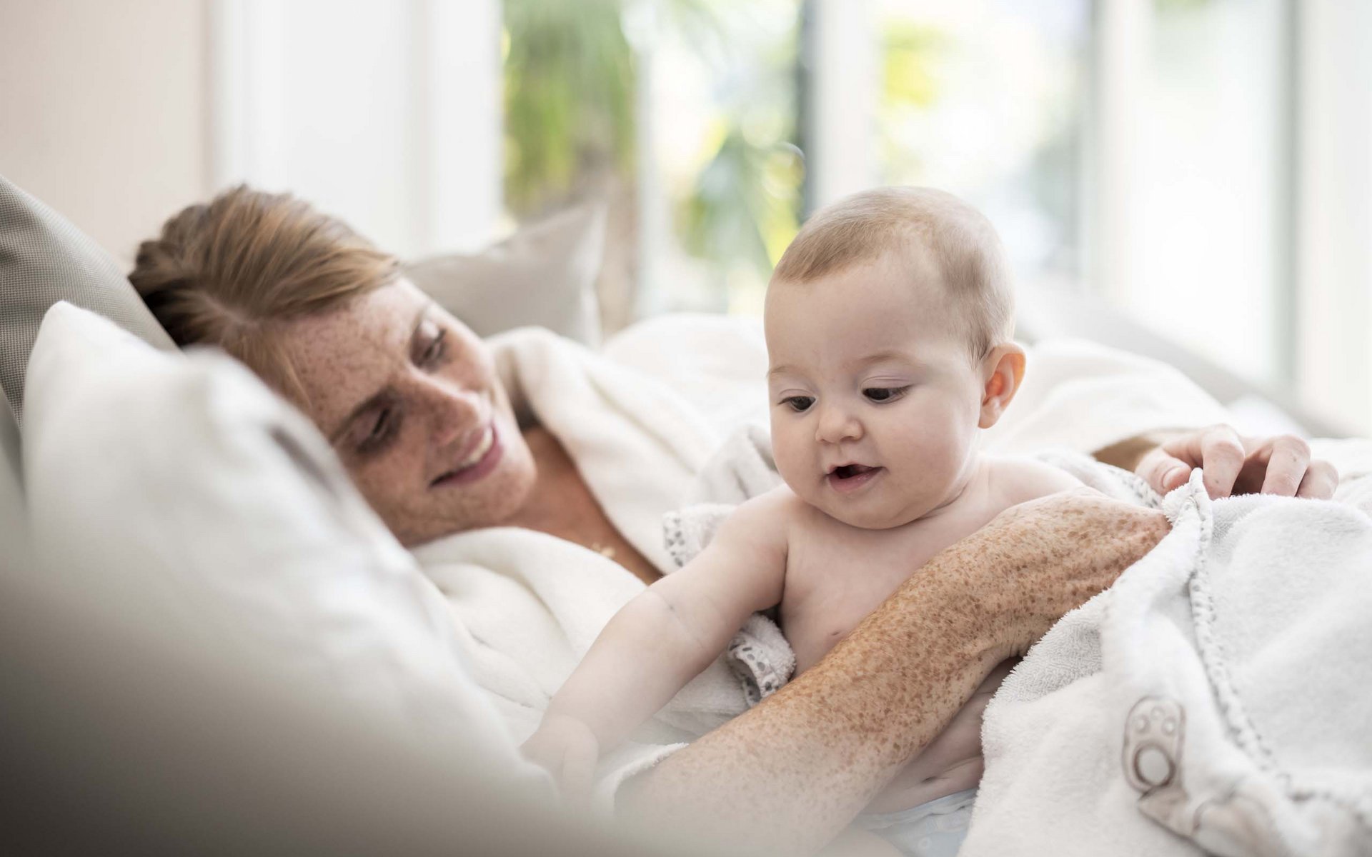 Mutter lächelt und hält Baby, beide in weißen Decken eingewickelt