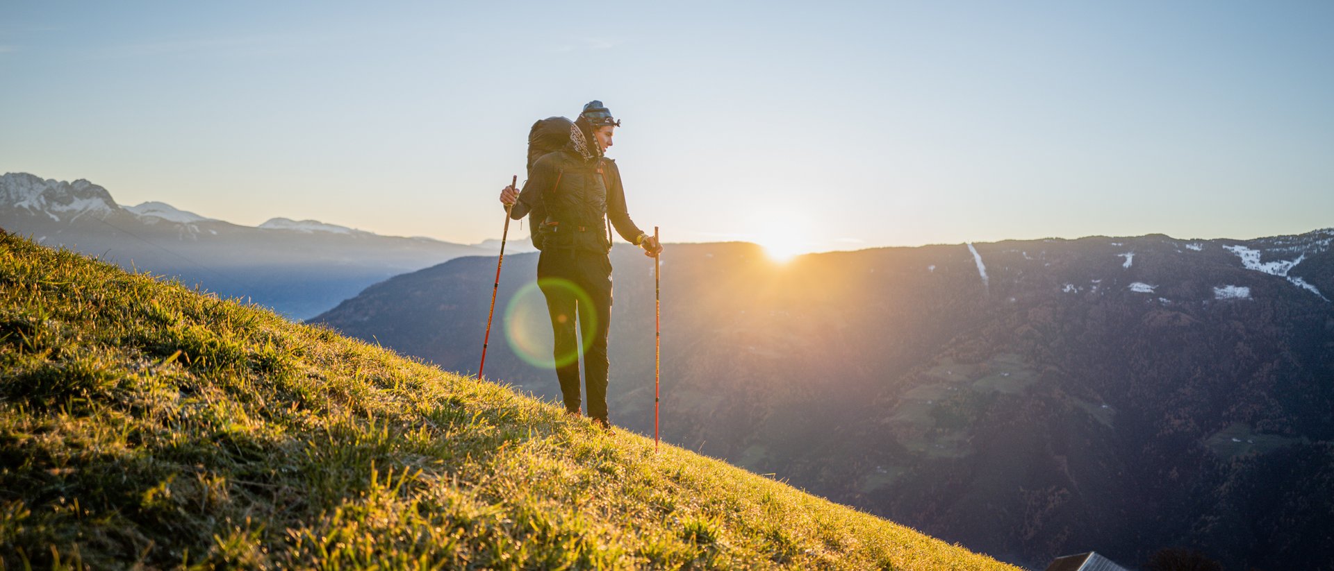 Wanderer mit Rucksack auf sonnigem Hügel mit Bergpanorama im Hintergrund