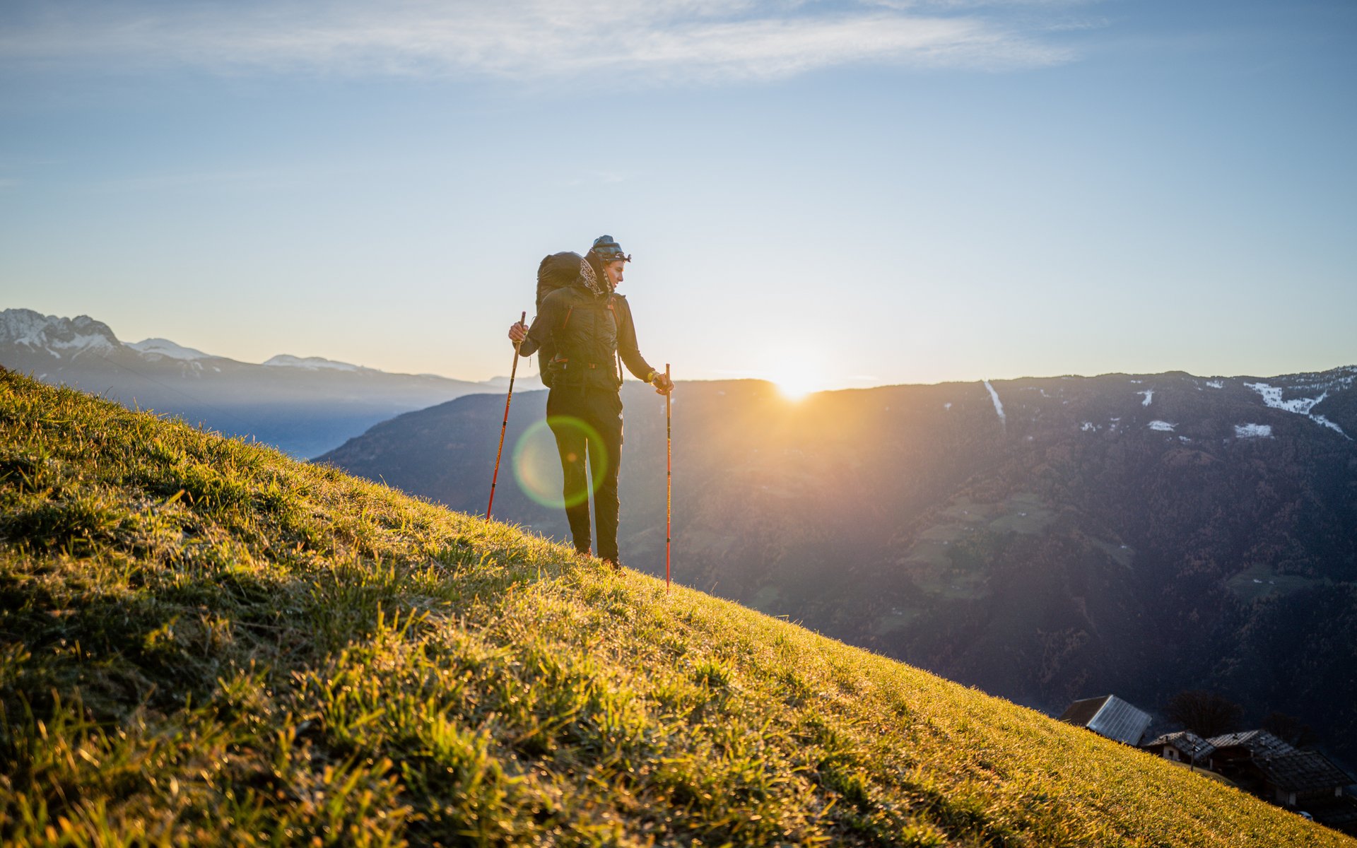 Wanderer mit Rucksack auf sonnigem Hügel mit Bergpanorama im Hintergrund