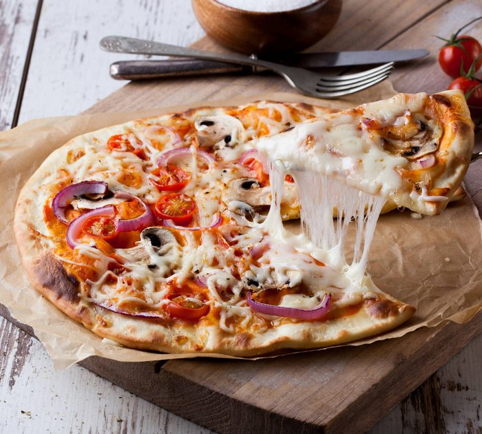 Fresh pizza with cheese, tomatoes, mushrooms, and onions on wooden board