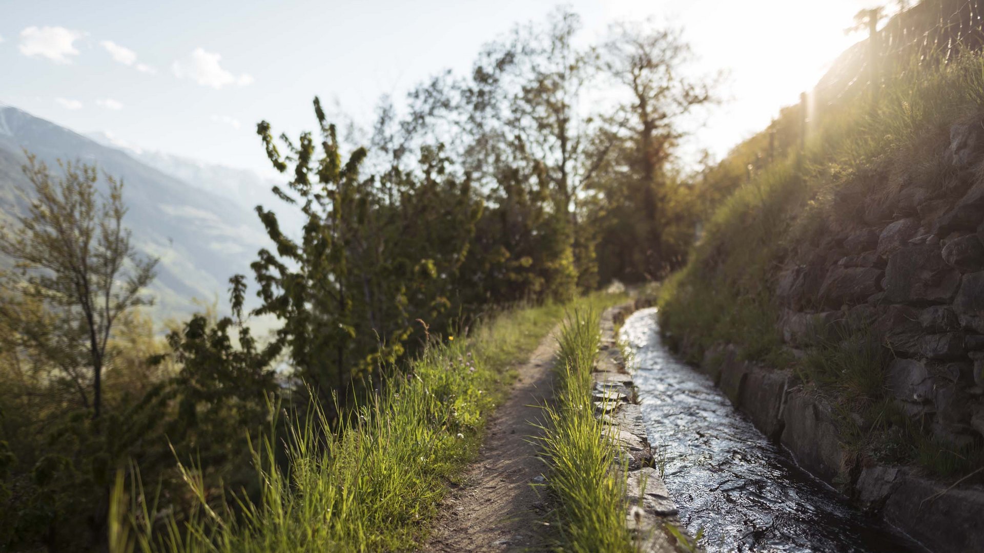 Wanderweg neben einem Wasserkanal mit sonnigem Bergblick