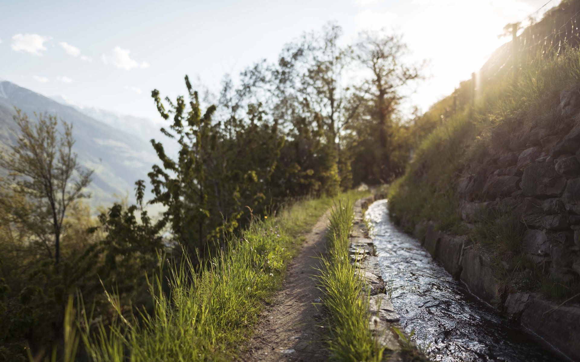 Wanderweg neben einem Wasserkanal mit sonnigem Bergblick